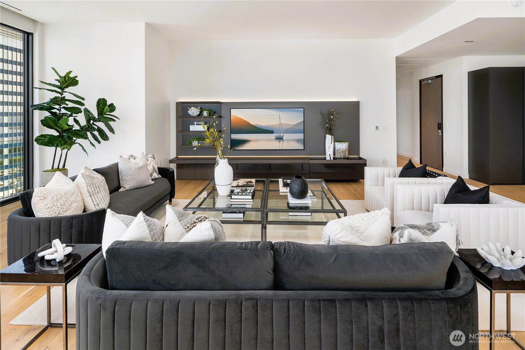 Staged living room with charcoal and white sofas, glass coffee tables, and floor-to-ceiling windows.