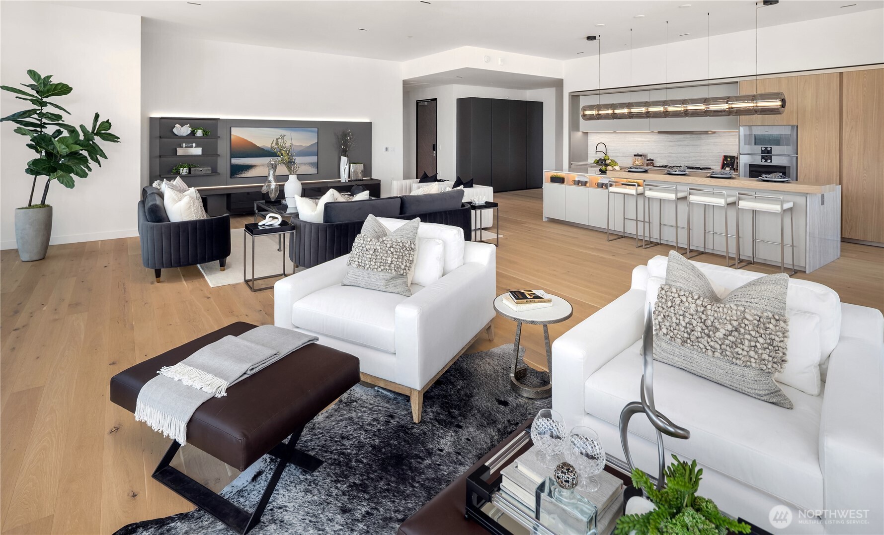 Open-plan living room and kitchen with a large island, wood cabinetry, and contrasting white and charcoal seating.