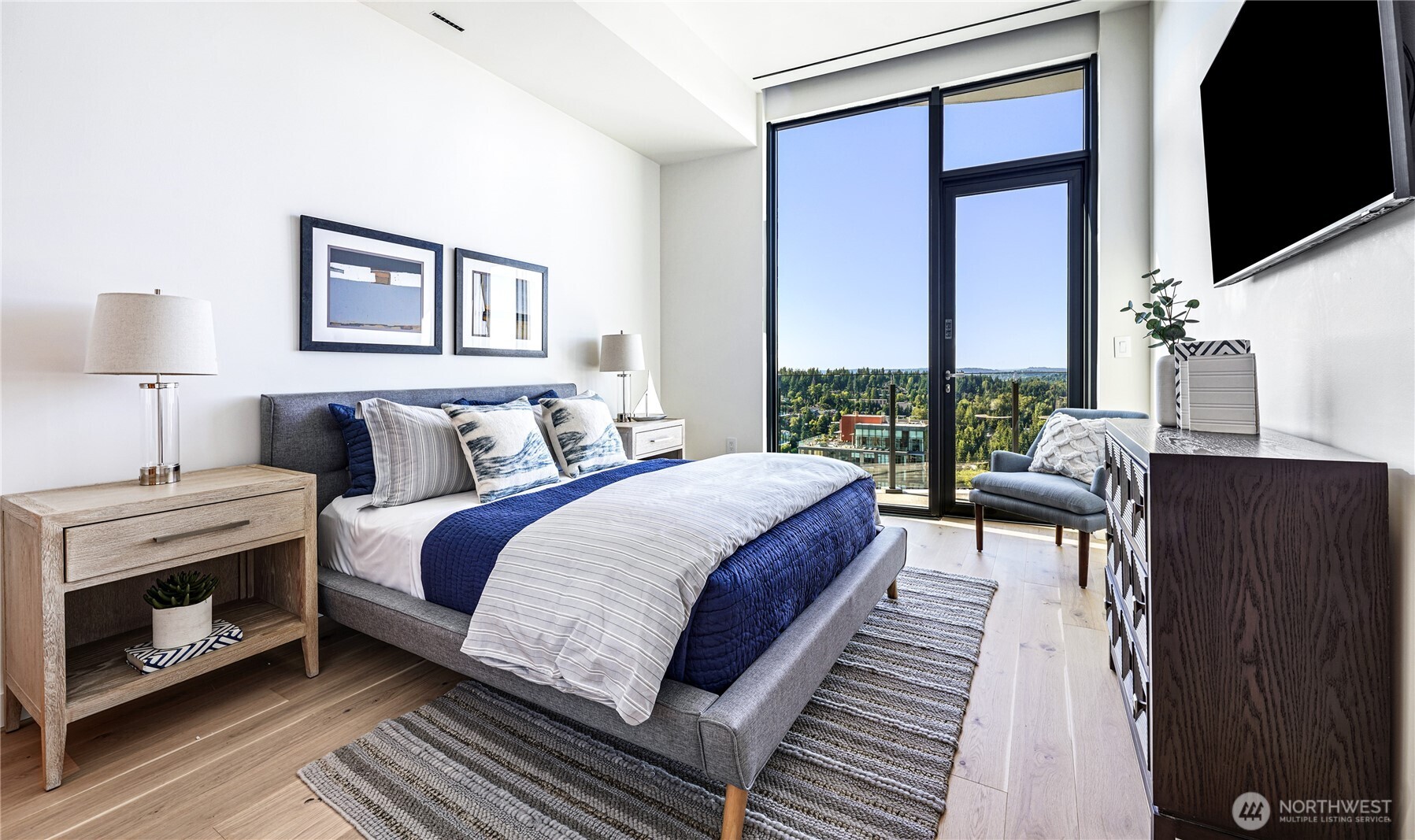 Staged bedroom with navy and white bedding, floor-to-ceiling windows, and a balcony view.