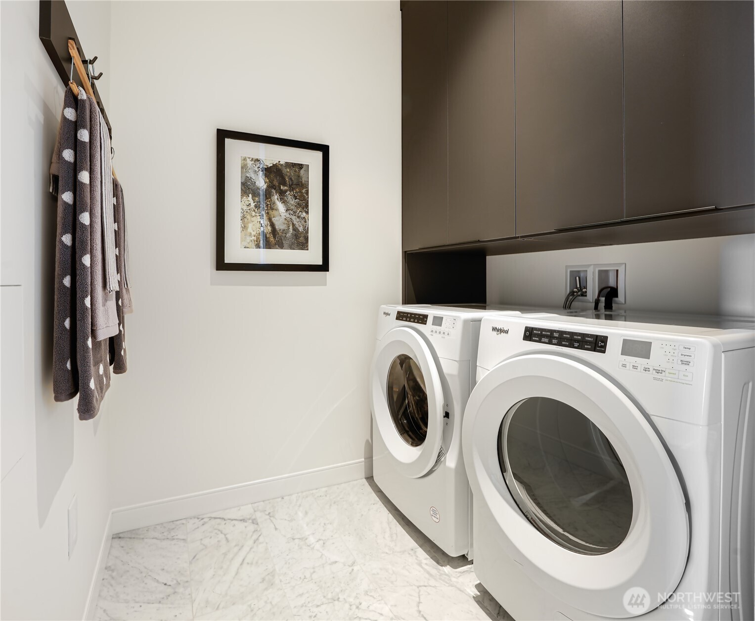 Laundry room with front-loading washer and dryer beneath dark cabinets.