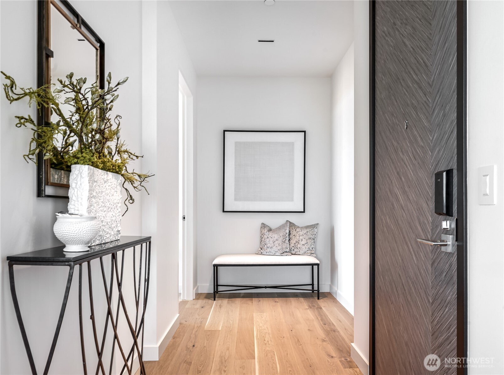 Entry foyer with a chevron-patterned front door, light wood floors, and a bench beneath framed art.