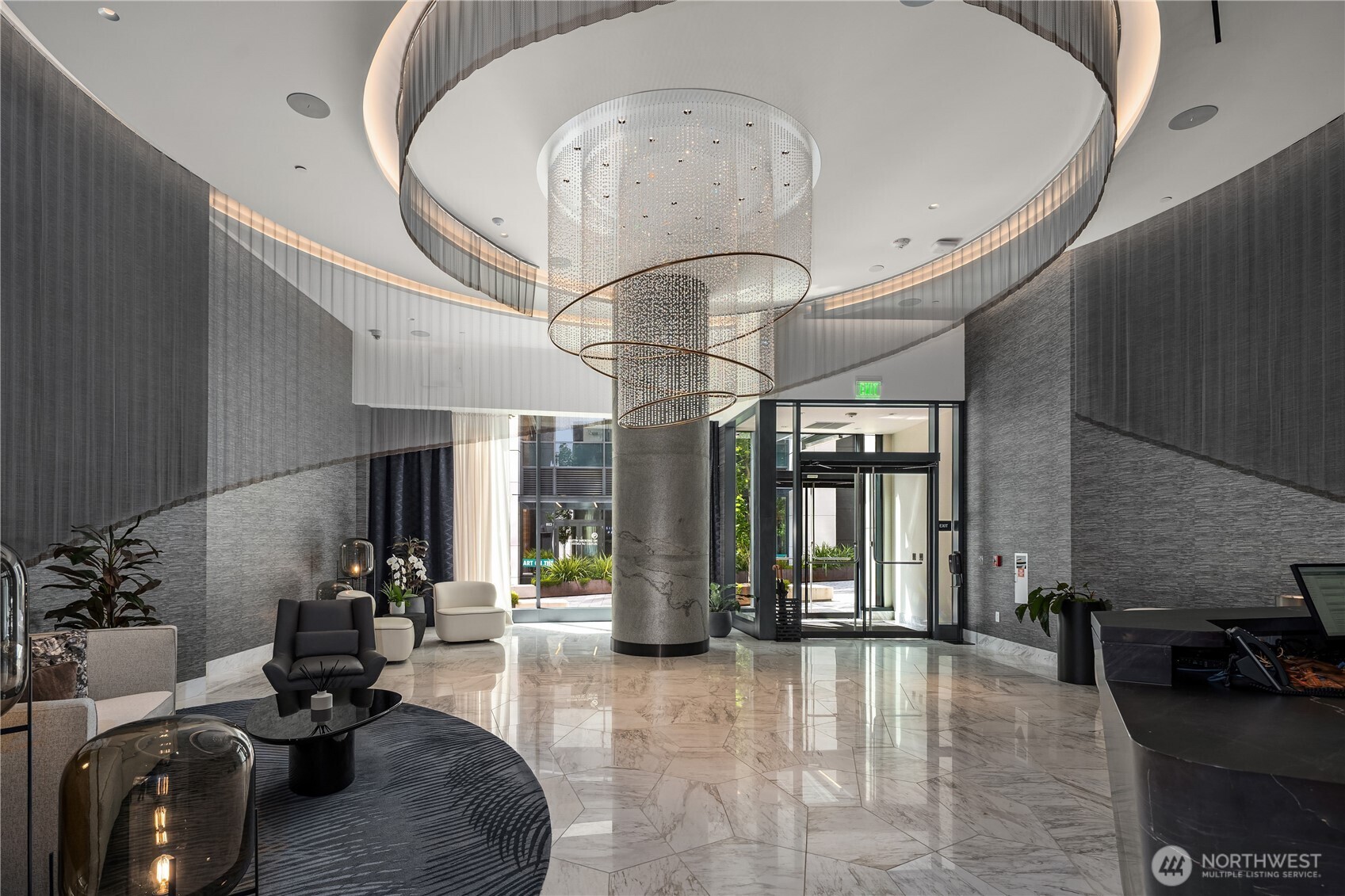 Modern condominium lobby with a large cylindrical chandelier, marble floors, and a stone column.