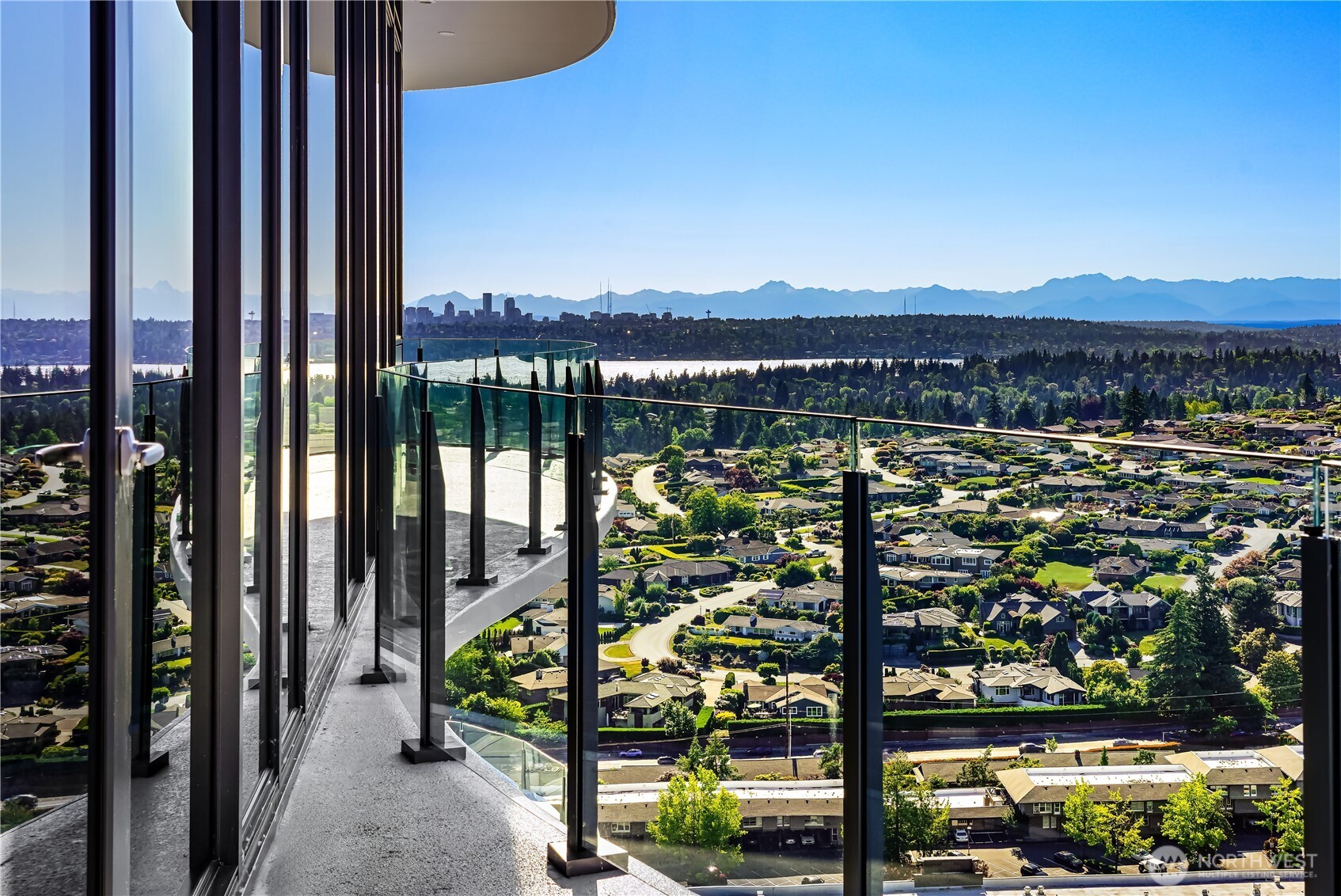 High-rise balcony overlooking a lake, Bellevue skyline, leafy neighborhoods, and distant mountains.
