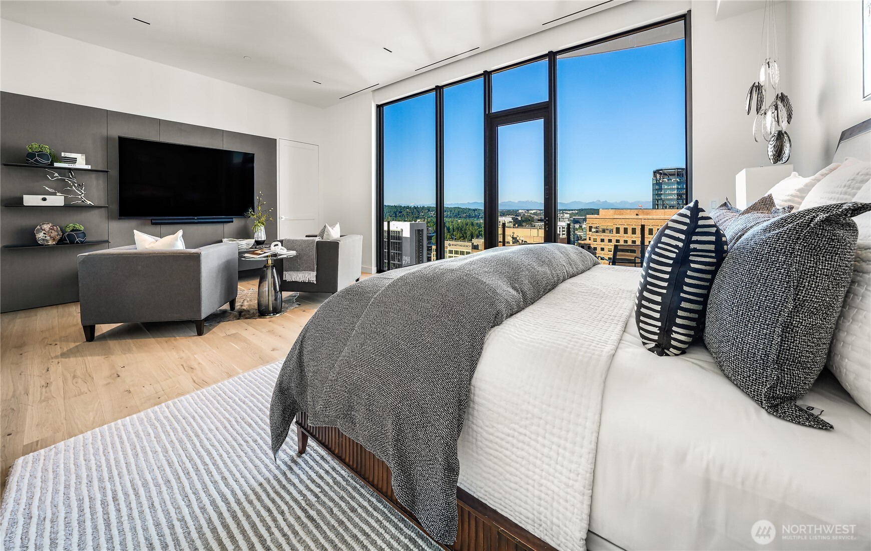 Staged bedroom with a sitting area and floor-to-ceiling windows overlooking Bellevue and distant mountains.