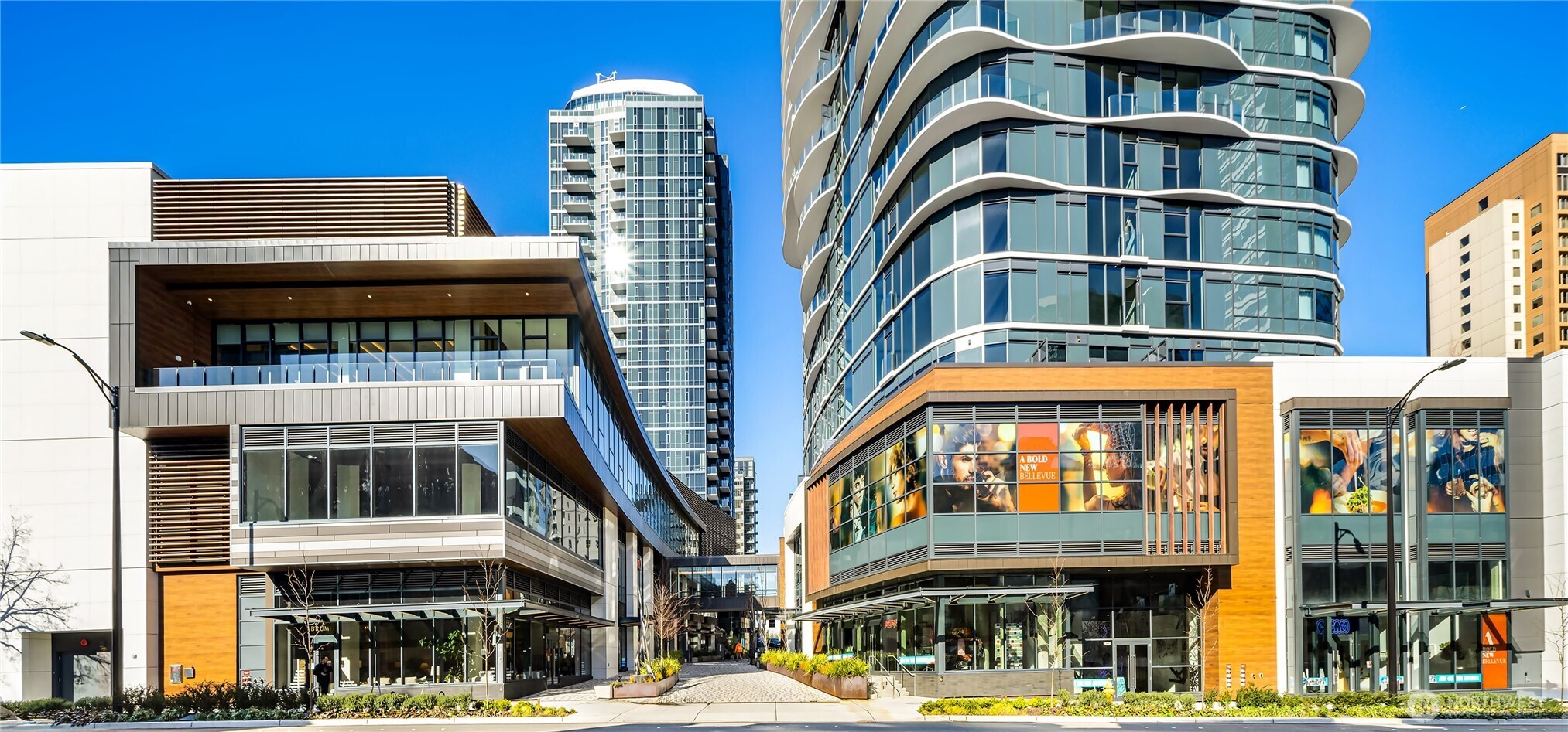Modern Bellevue high-rise development with curved glass towers, retail storefronts, and a landscaped pedestrian courtyard.