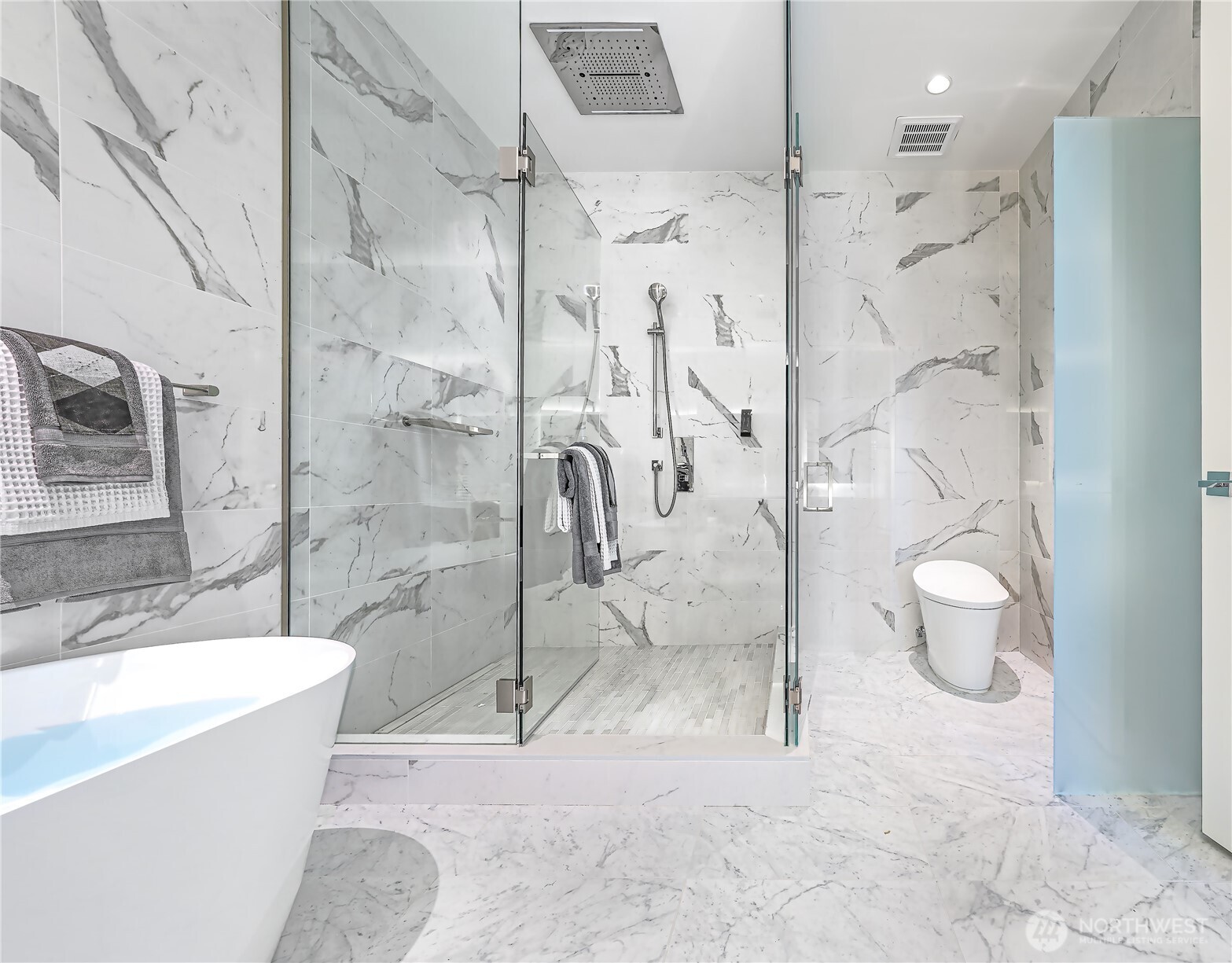Marble-tiled bathroom with a glass shower, rain showerhead, freestanding tub, and white toilet.