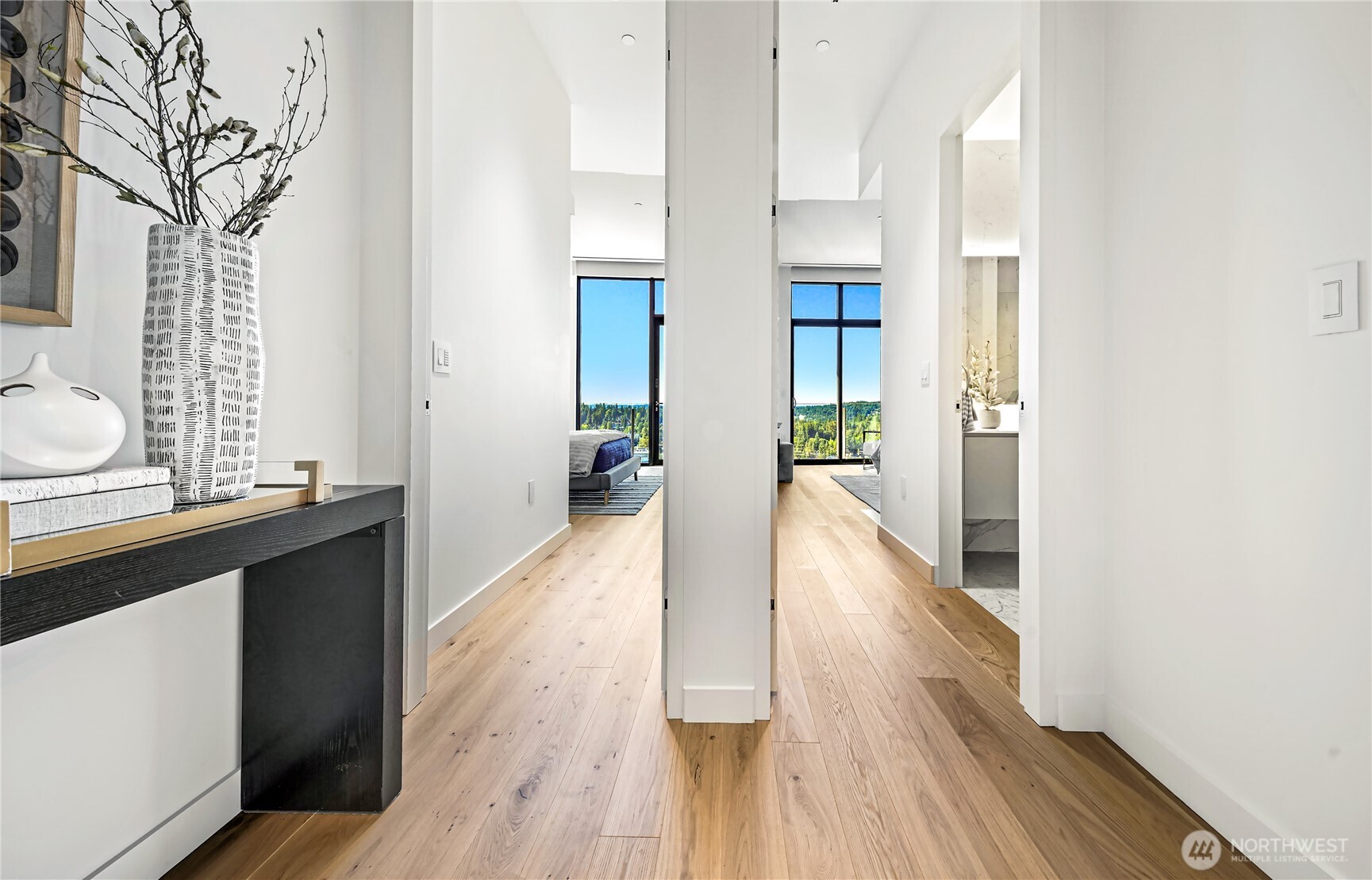 Condo hallway with wide-plank wood floors and bedroom windows overlooking wooded greenery.