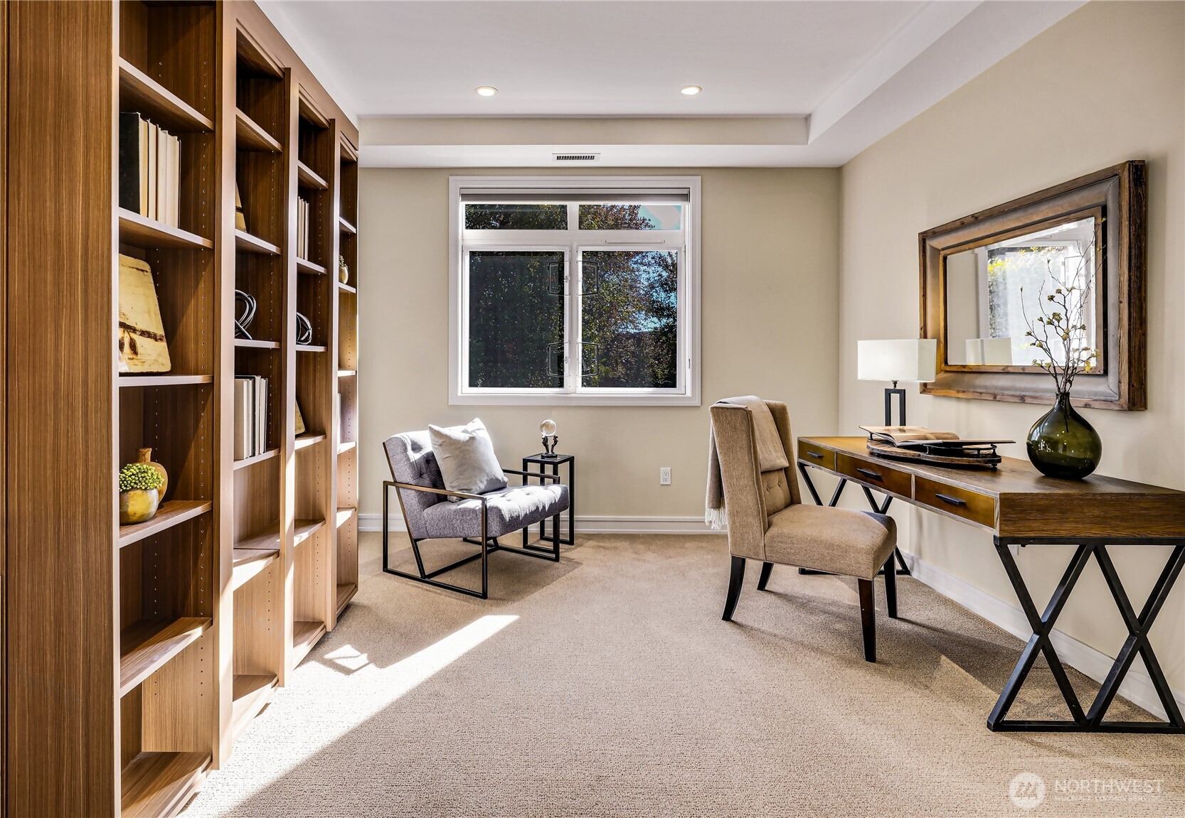 Furnished home office with built-in wooden bookshelves, a desk, and sunlight through the window.