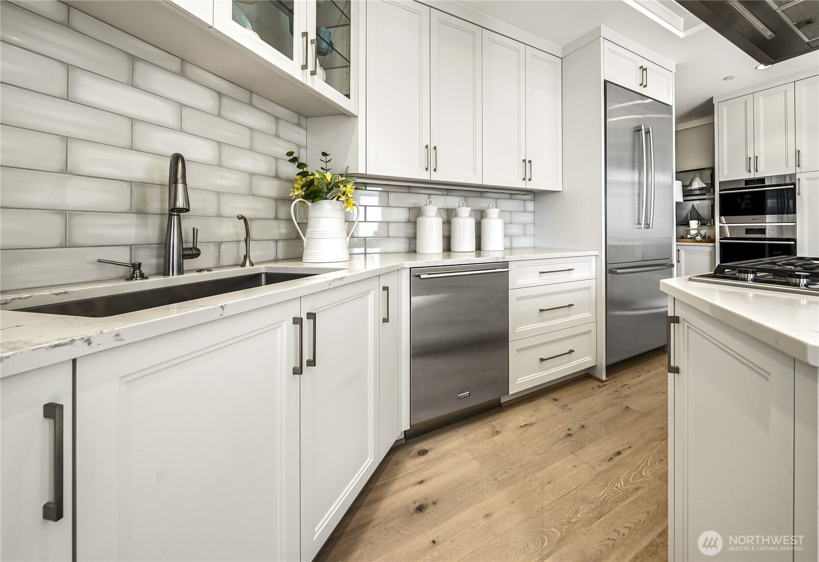 Kitchen with white cabinetry, a subway tile backsplash, stainless steel appliances, and wood flooring.