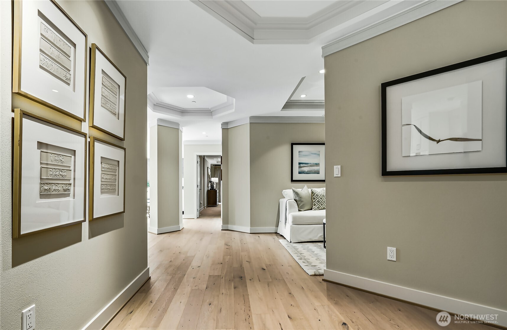 Condo entry hallway with light wood floors, framed artwork, and a glimpse of the living room.