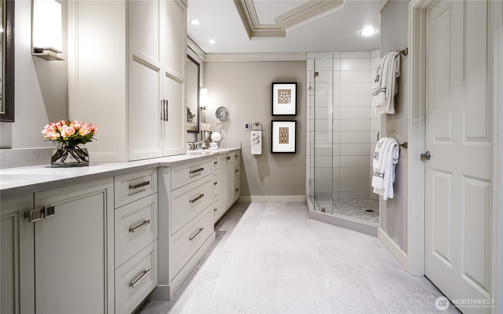 Renovated bathroom with a long white vanity and glass-enclosed walk-in shower.