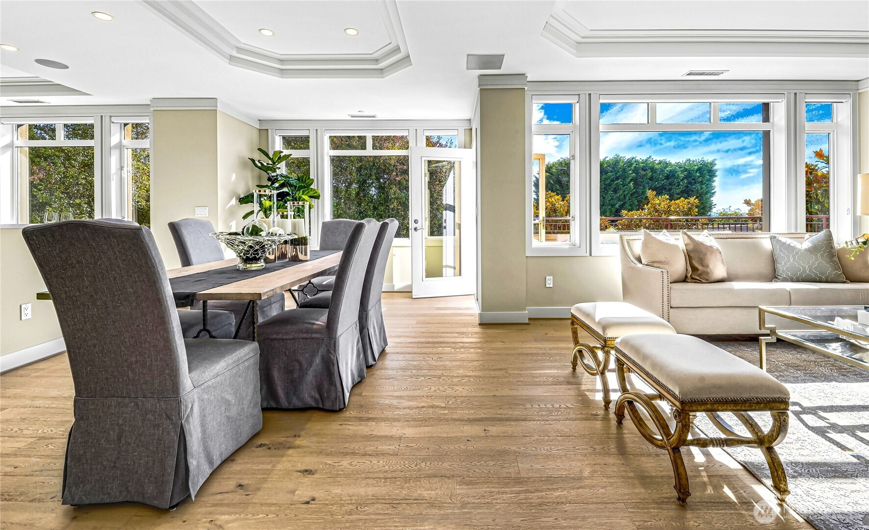 Open-plan living and dining room with wide-plank floors and large windows overlooking trees.