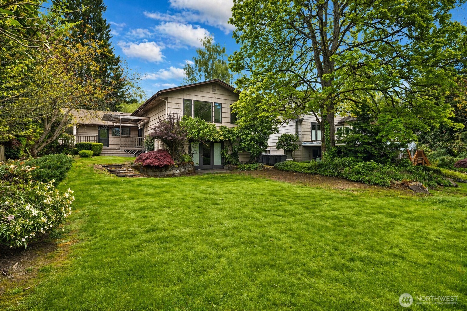Home’s rear exterior beyond a broad lawn, framed by mature trees and landscaped garden beds.