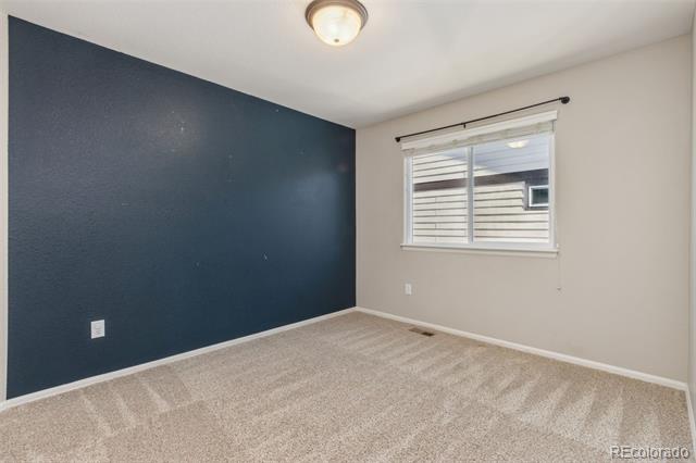 Empty bedroom with a dark blue accent wall, beige carpet, and a window with blinds.