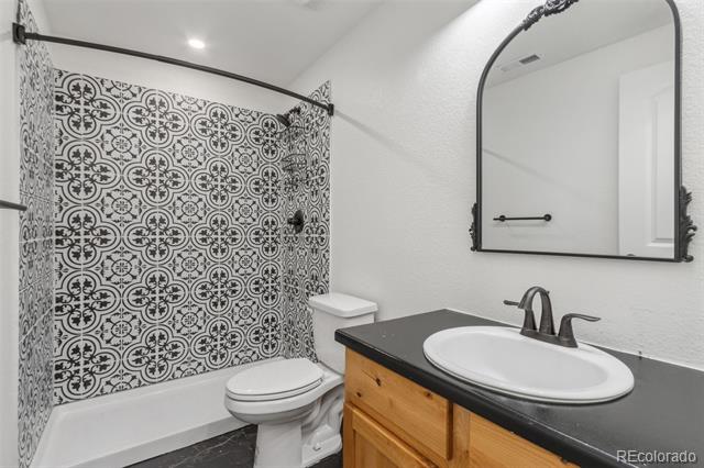 Bathroom with patterned black-and-white shower tile, a wood vanity, and an arched mirror.