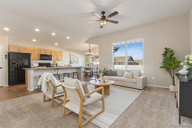 Open-plan living room and kitchen with a beige sectional, wood-framed chairs, and large windows.