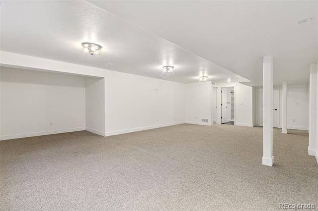 Finished basement with beige carpet, white walls, and several support columns.