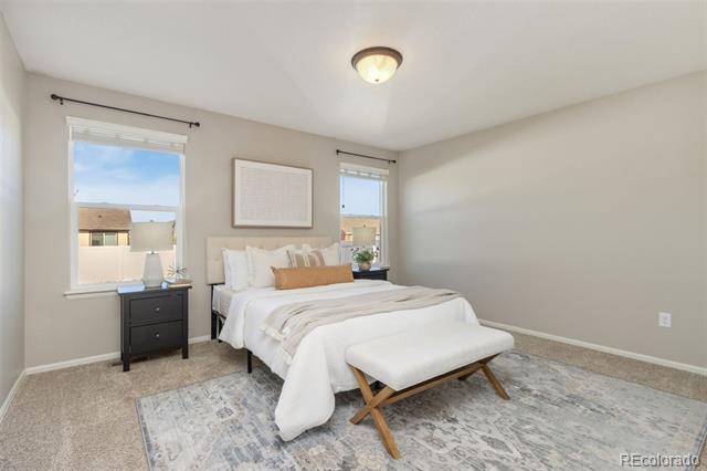 Staged bedroom with a white bed, tan accent pillow, and upholstered bench on a patterned rug.