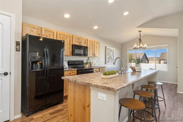 Kitchen with wood cabinets, black appliances, and a granite island with bar stools.