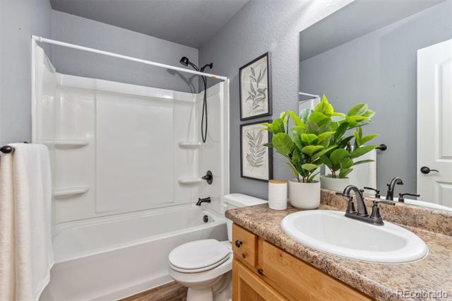Bathroom with a white tub and shower, toilet, and wood vanity topped with granite and a leafy plant.