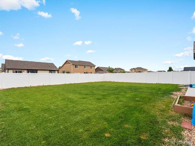 Backyard with a broad green lawn, white privacy fence, and raised garden planter.