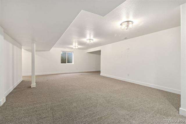 Finished basement room with beige carpet, a small window, ceiling lights, and a support column.