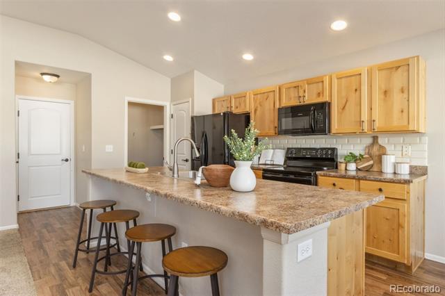 Kitchen with a granite-topped island and seating, natural wood cabinets, and black appliances.