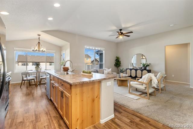 Open kitchen with a wood-paneled island and stone countertop adjoining a dining area and furnished living room.