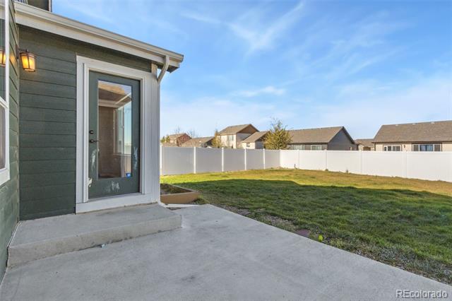 Backyard patio beside a dark-sided home, overlooking a grassy yard enclosed by a white fence.