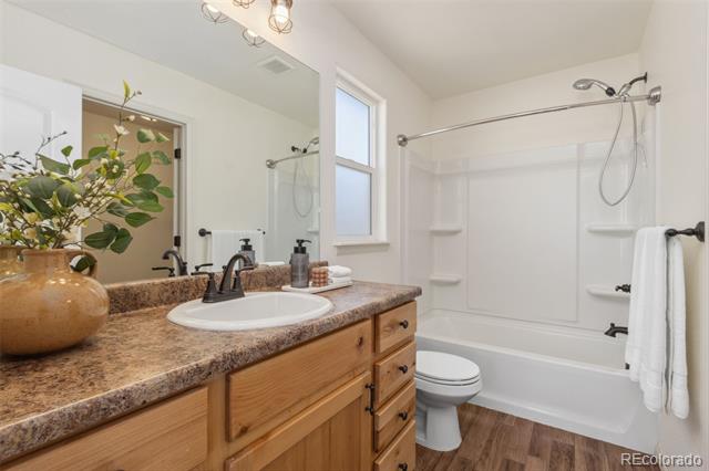 Bathroom with a wood vanity and brown countertop beside a white tub-shower enclosure.