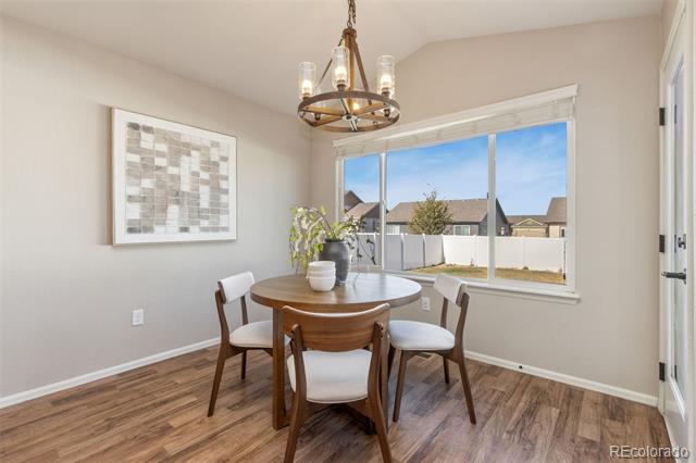 Dining area with a round wooden table, chandelier, and large window overlooking a fenced backyard.
