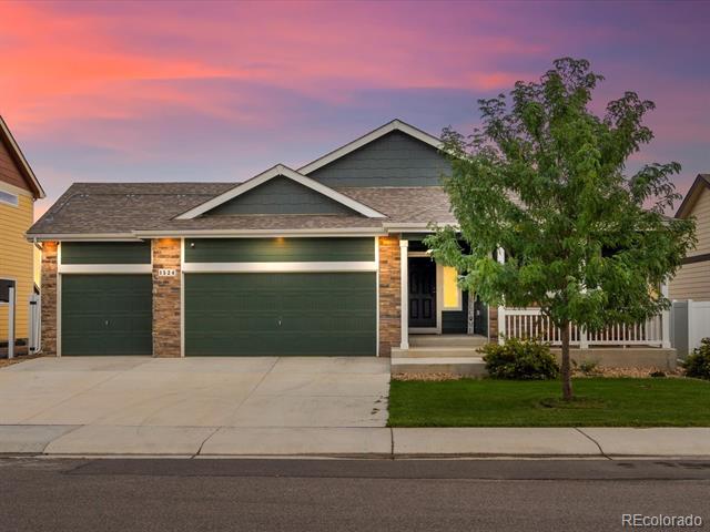 Single-story home with two green garage doors, brick accents, and a covered porch at dusk.