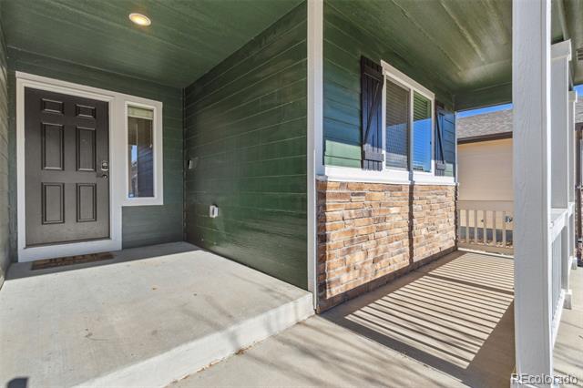Covered front porch with a dark gray door, green siding, and stone veneer.