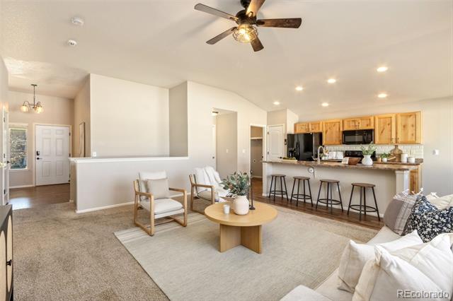 Open-plan living room and kitchen with a bar island, light wood cabinets, and a ceiling fan.