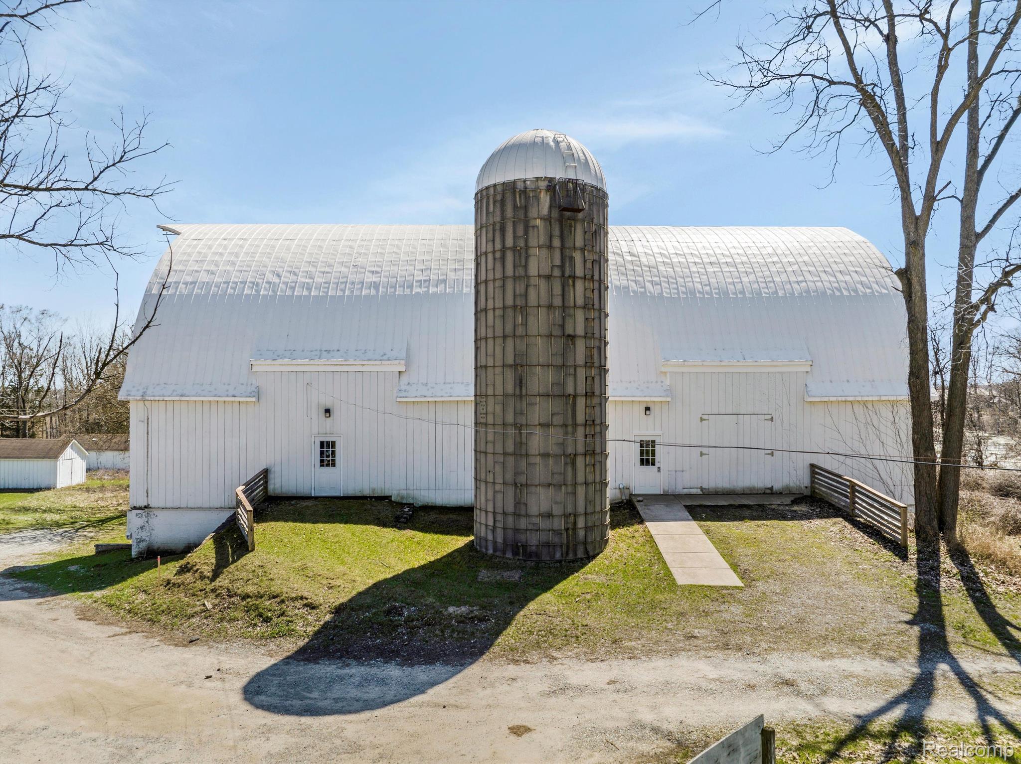White barn with a tall central silo, walkway, and grassy yard.