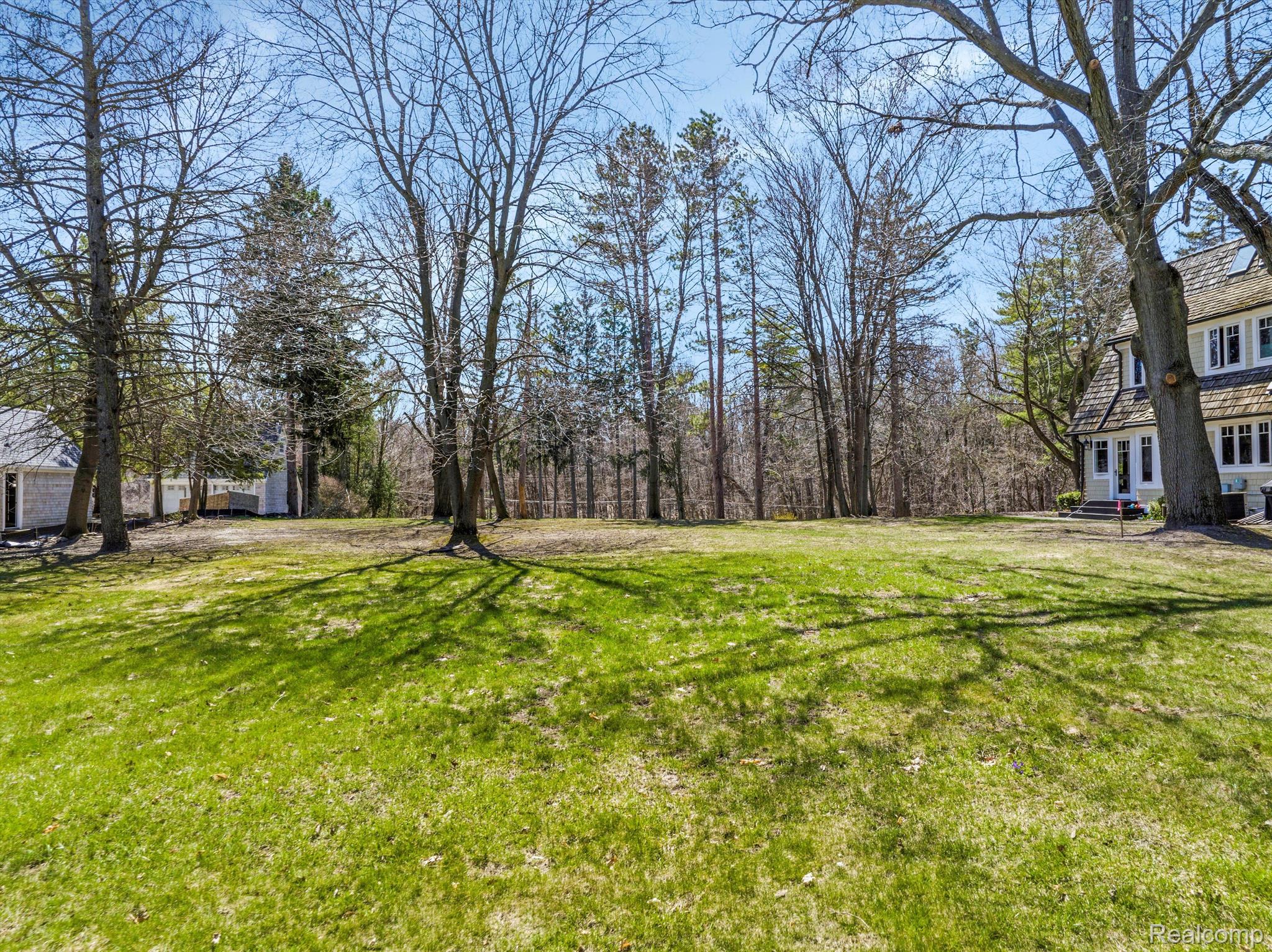 Grassy yard with mature trees and part of a shingle-sided house.