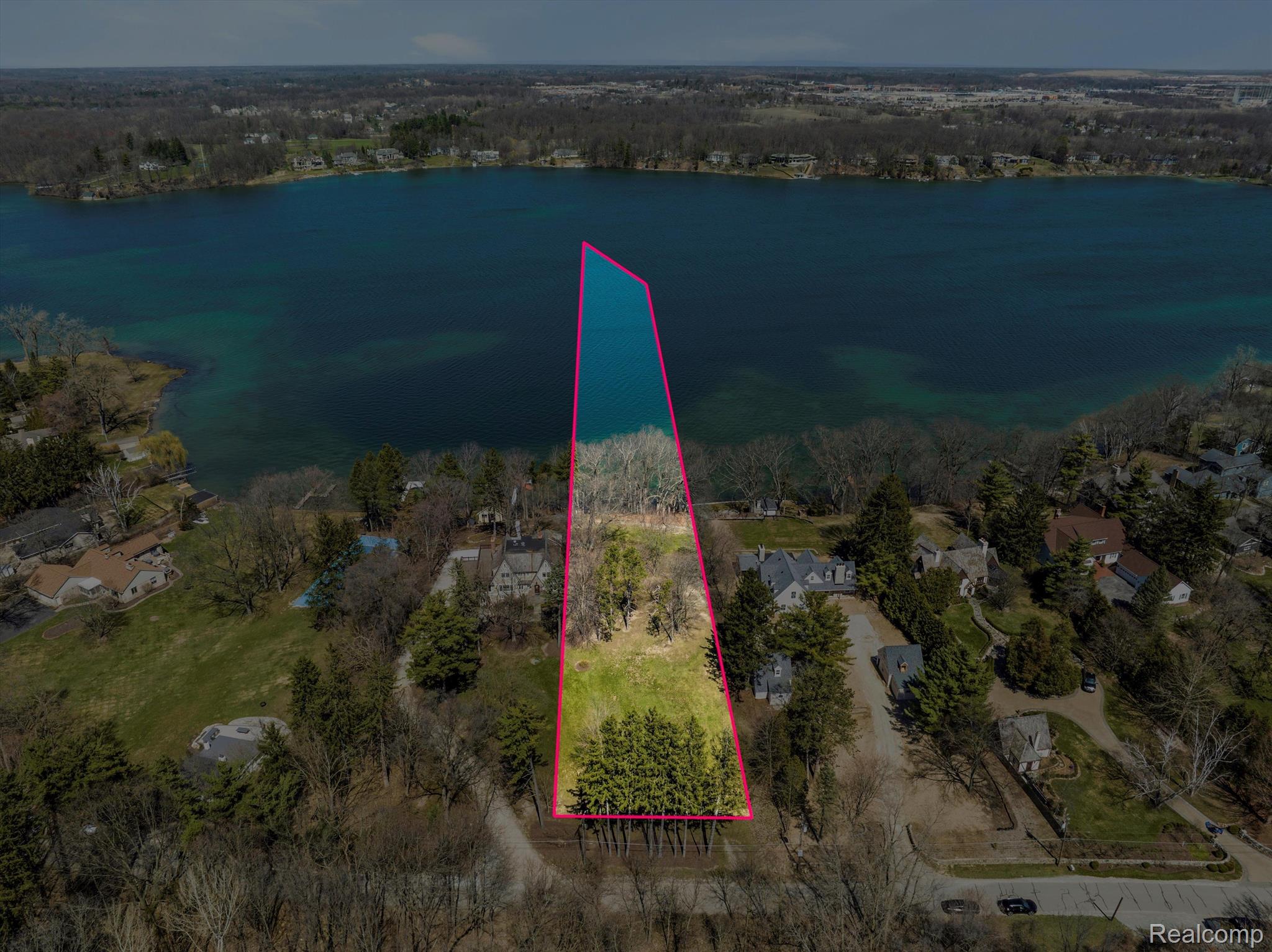 Aerial view of a wooded lakeside parcel outlined in pink, extending from the street to the water.