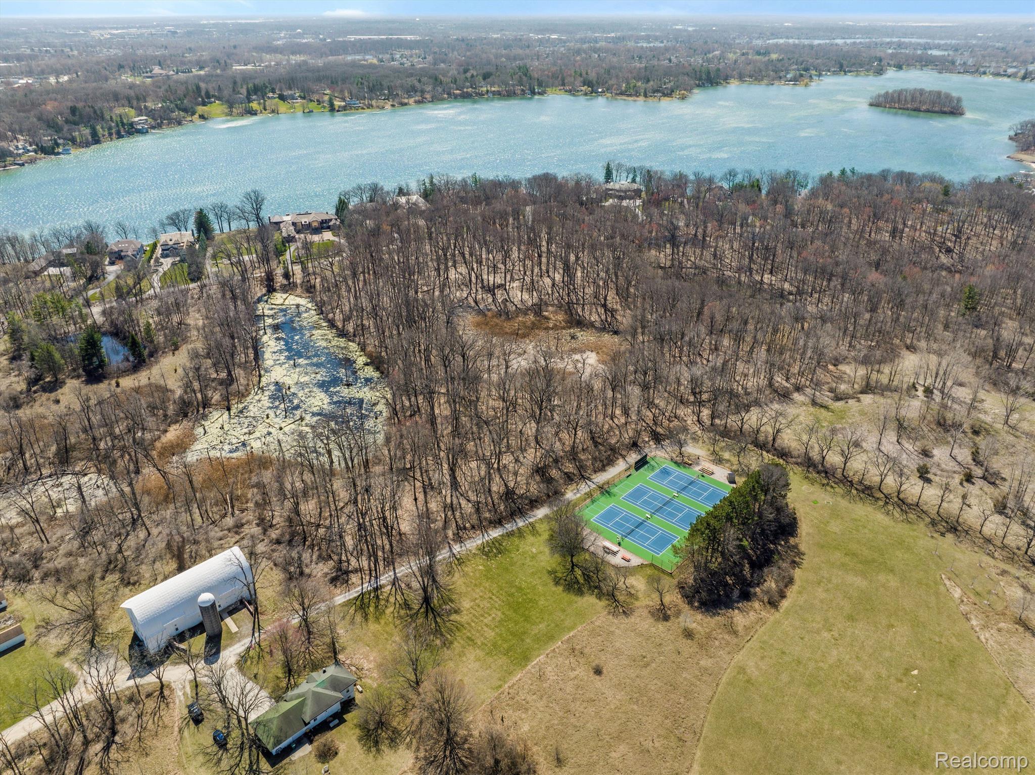 Aerial view of wooded Lake Angelus shoreline, tennis courts, and open grounds.