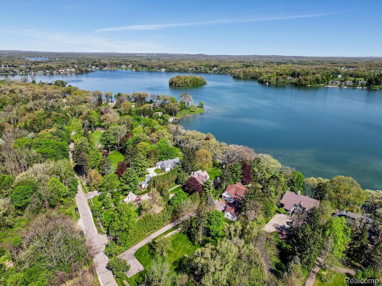 Aerial view of Lake Angelus, with a wooded island and homes along the shoreline.