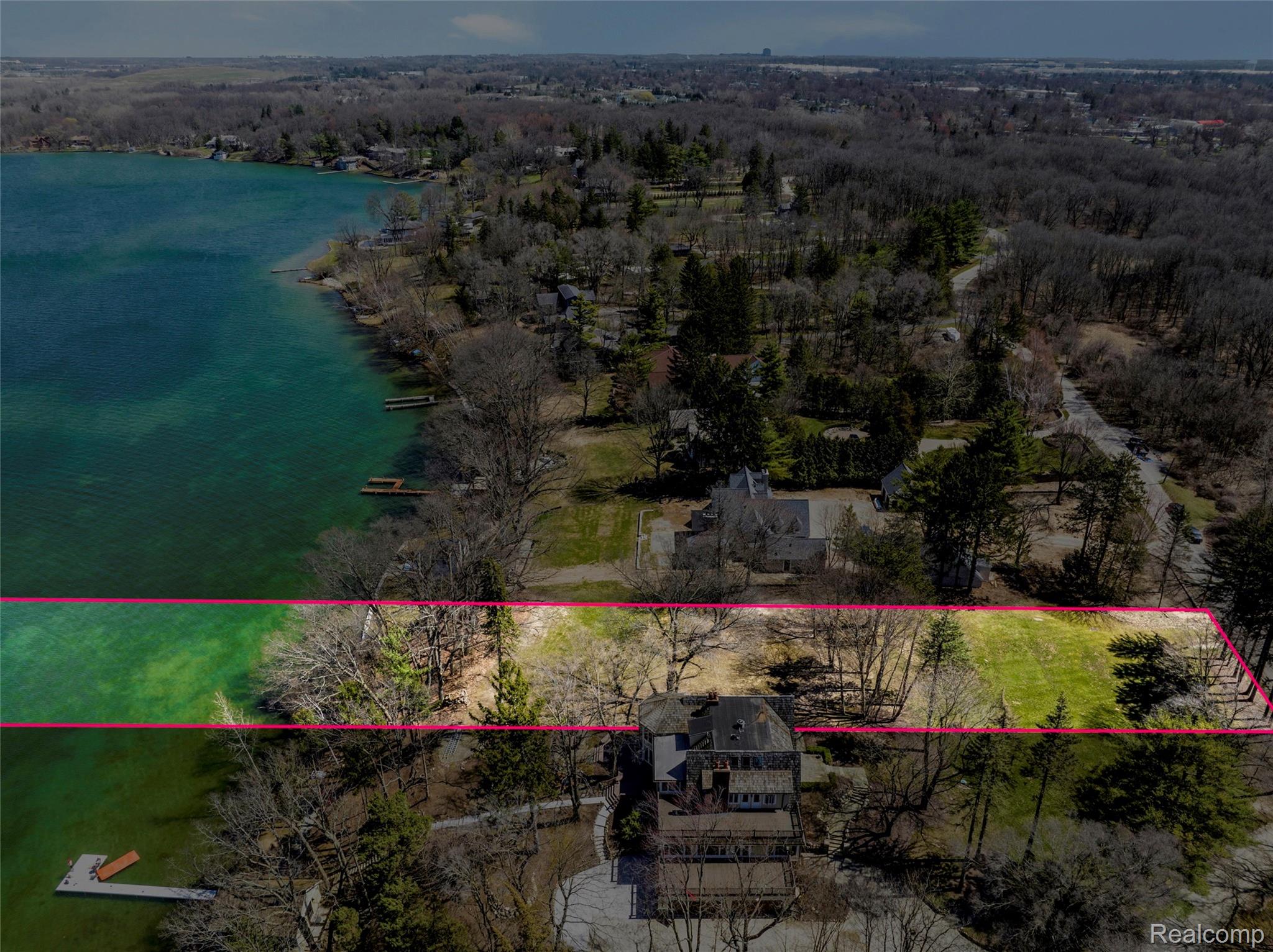 Aerial view of a wooded Lake Angelus waterfront lot outlined in pink, with a house and dock.