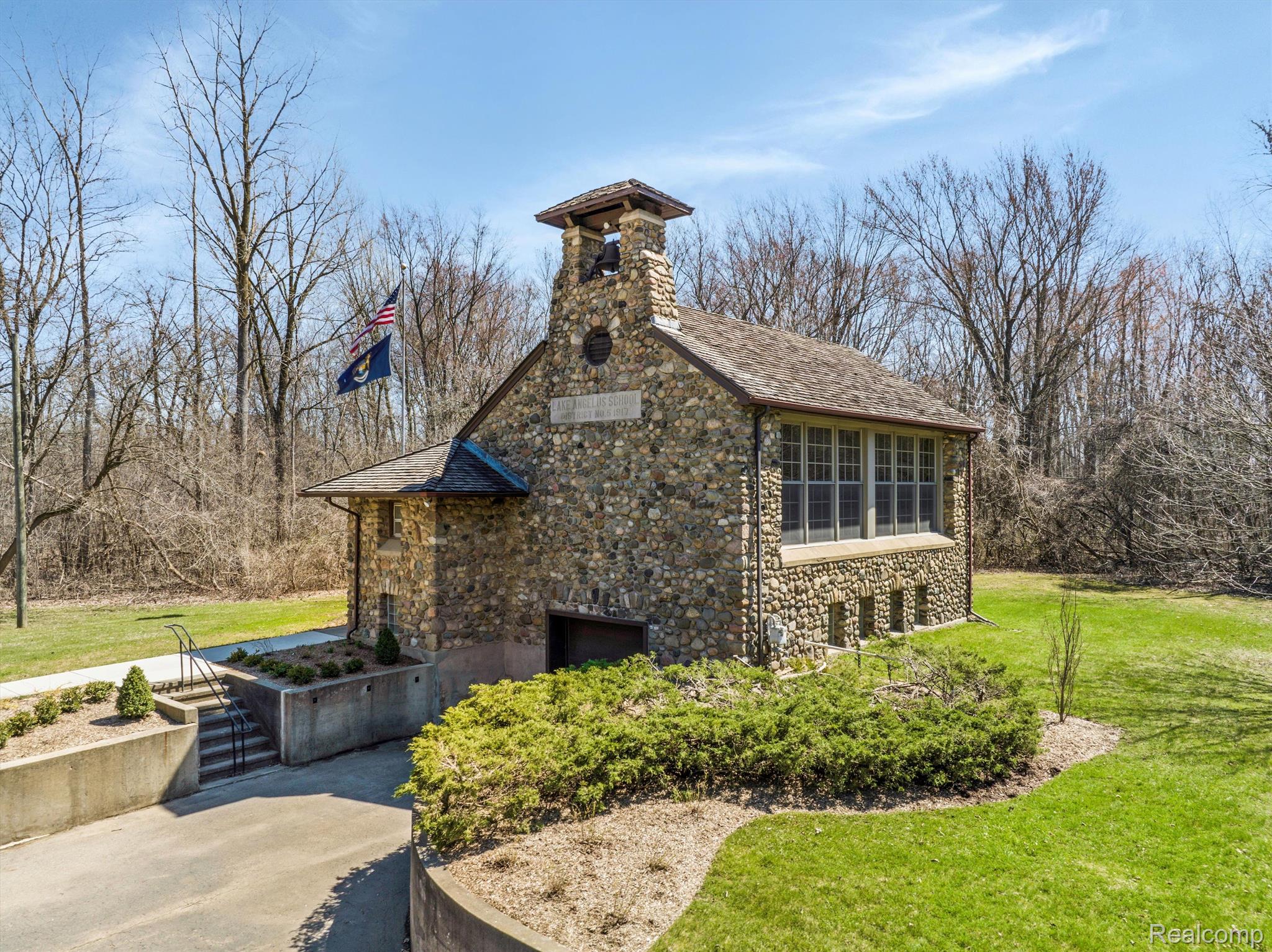 Stone school building with a bell tower and large windows, surrounded by leafless trees.