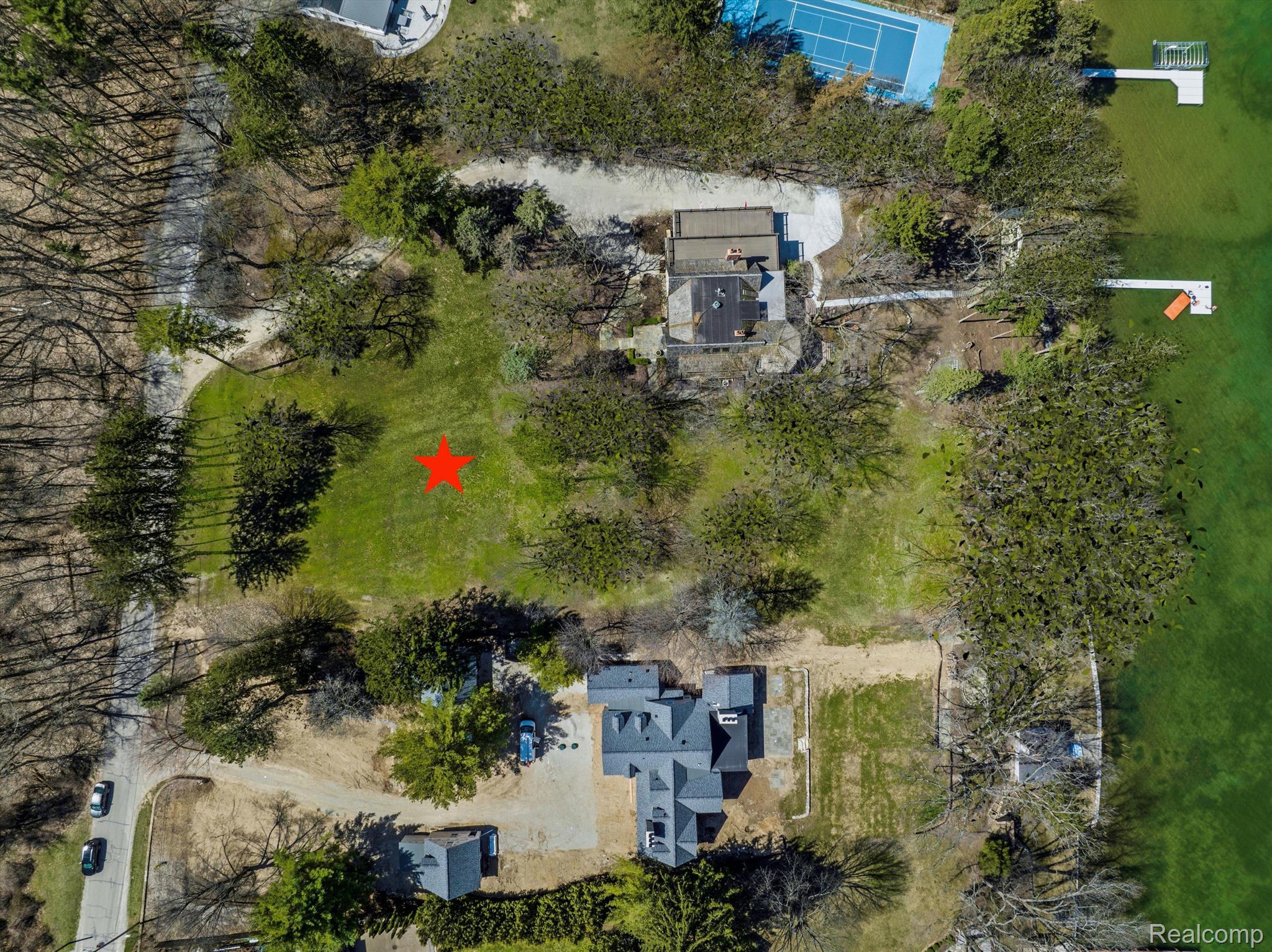Aerial view of a grassy lakeside lot marked with a red star, near a tennis court and dock.