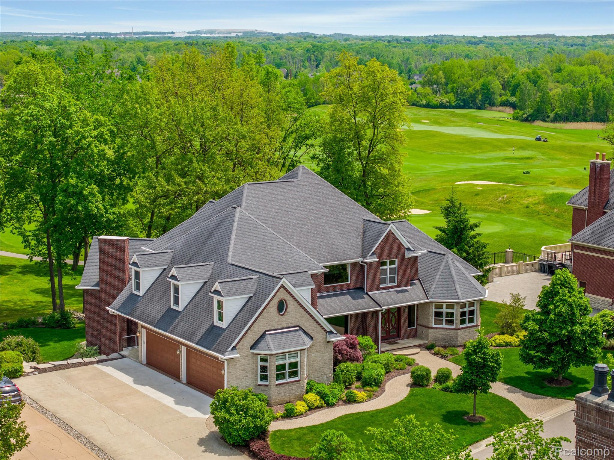 Aerial view of a brick home beside a golf course, with landscaped grounds and a broad driveway.