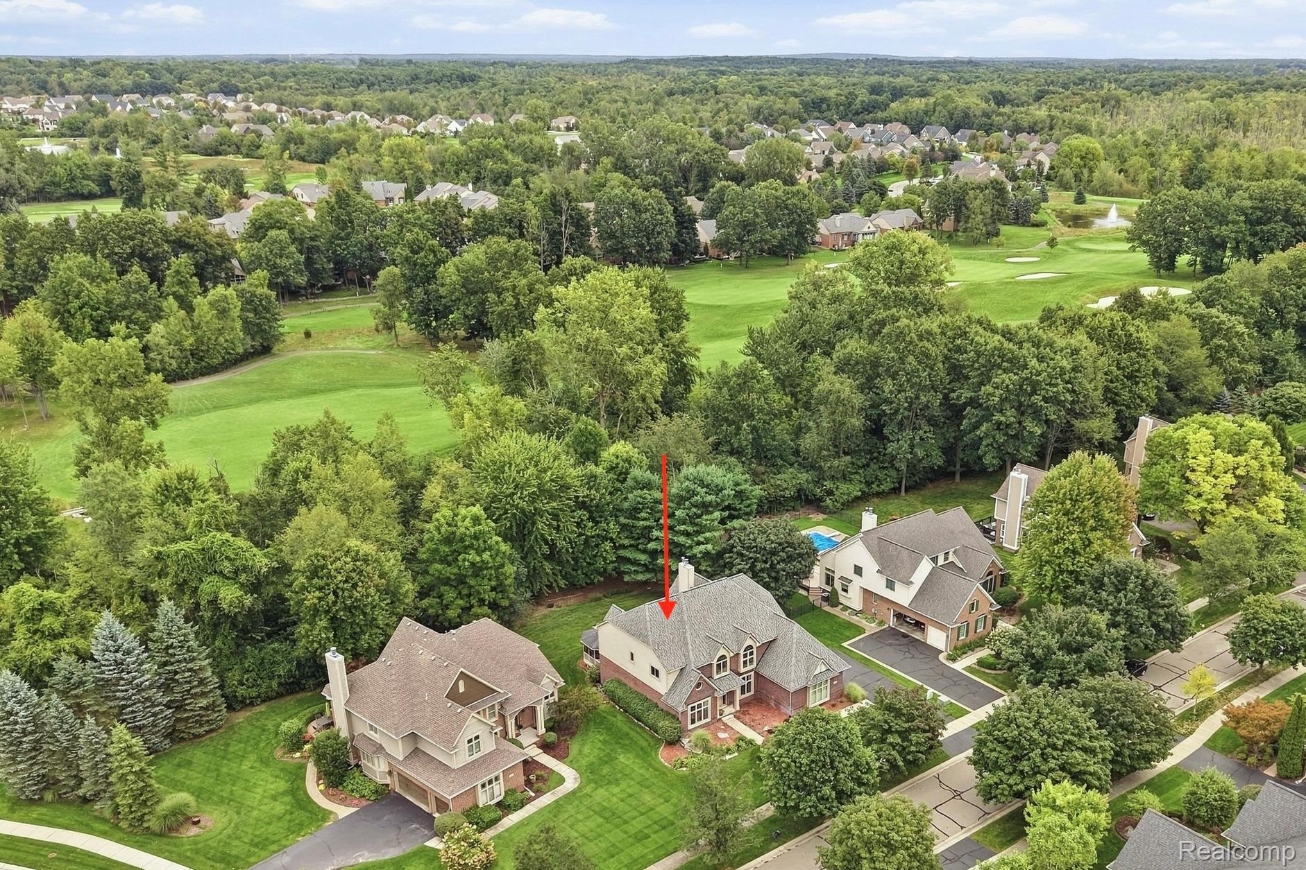 Aerial view of the home beside wooded lots and golf course fairways, marked by a red arrow.