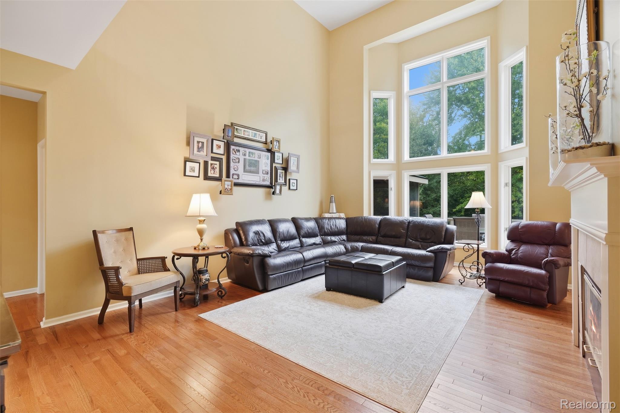 Living room with a leather sectional, tall windows, hardwood floors, and a fireplace.