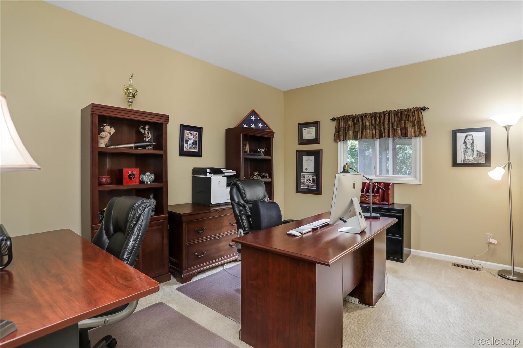 Furnished home office with wooden desks, leather chairs, dark bookcases, and a window.