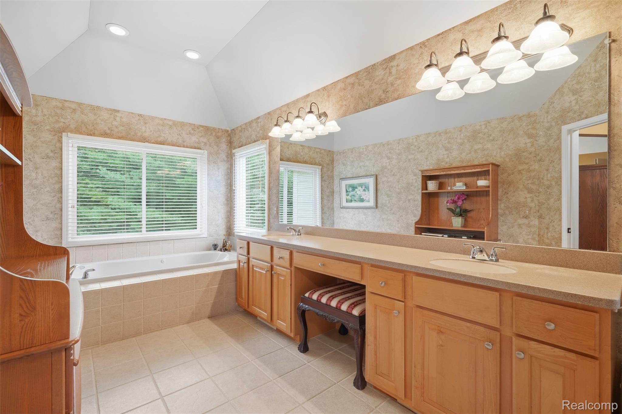 Bathroom with soaking tub and long double-sink wood vanity beneath a vaulted ceiling.