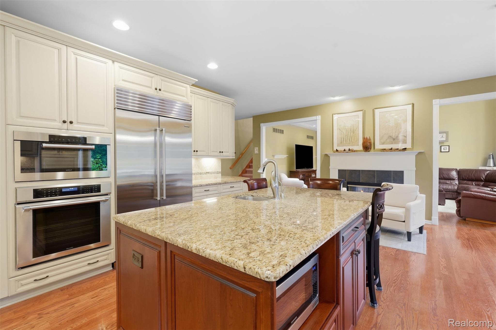 Kitchen with cream cabinetry, stainless-steel appliances, and a large granite-topped island opening to a living room.