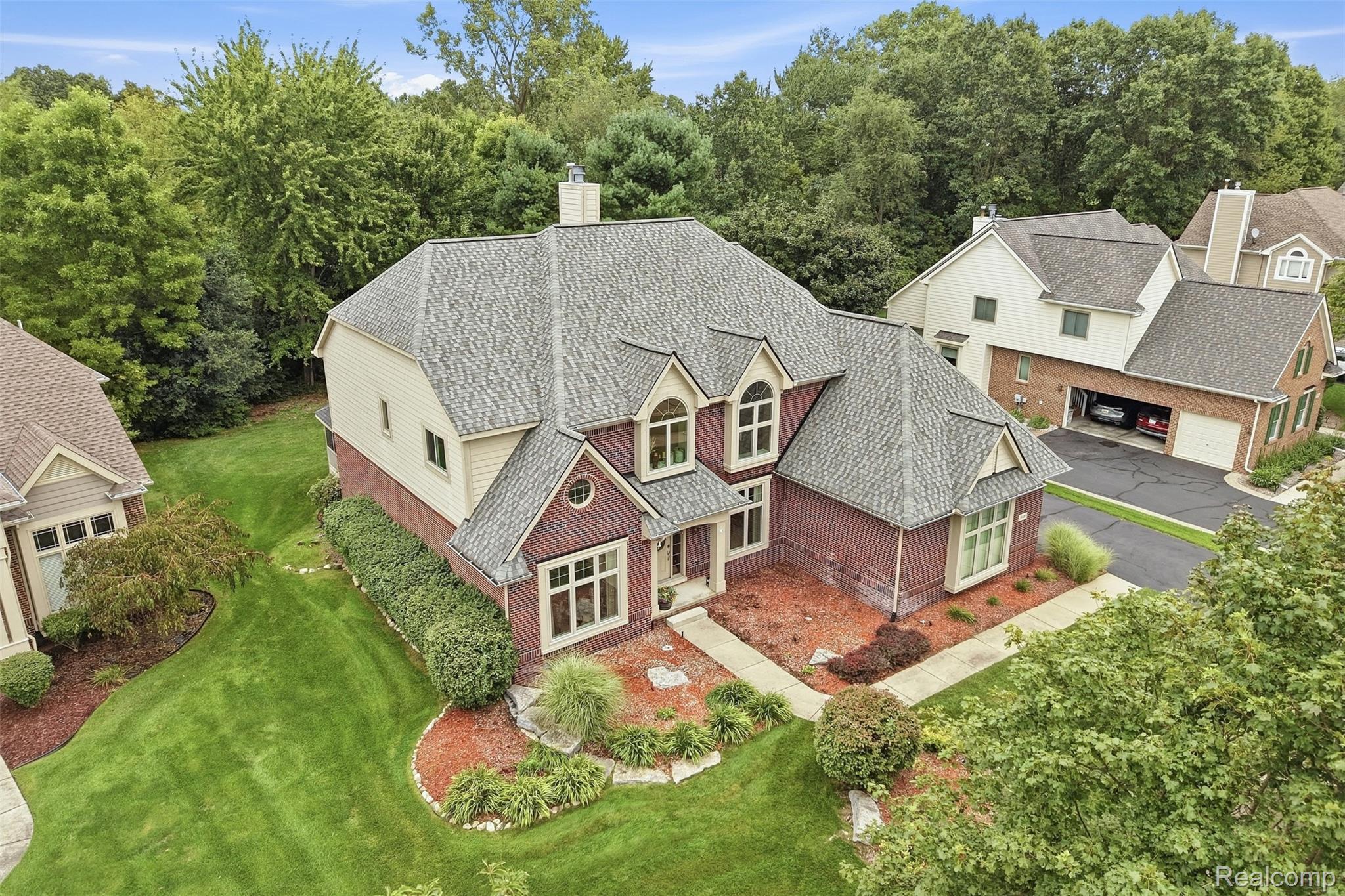 Aerial view of a brick-and-cream home with landscaped grounds and mature trees.