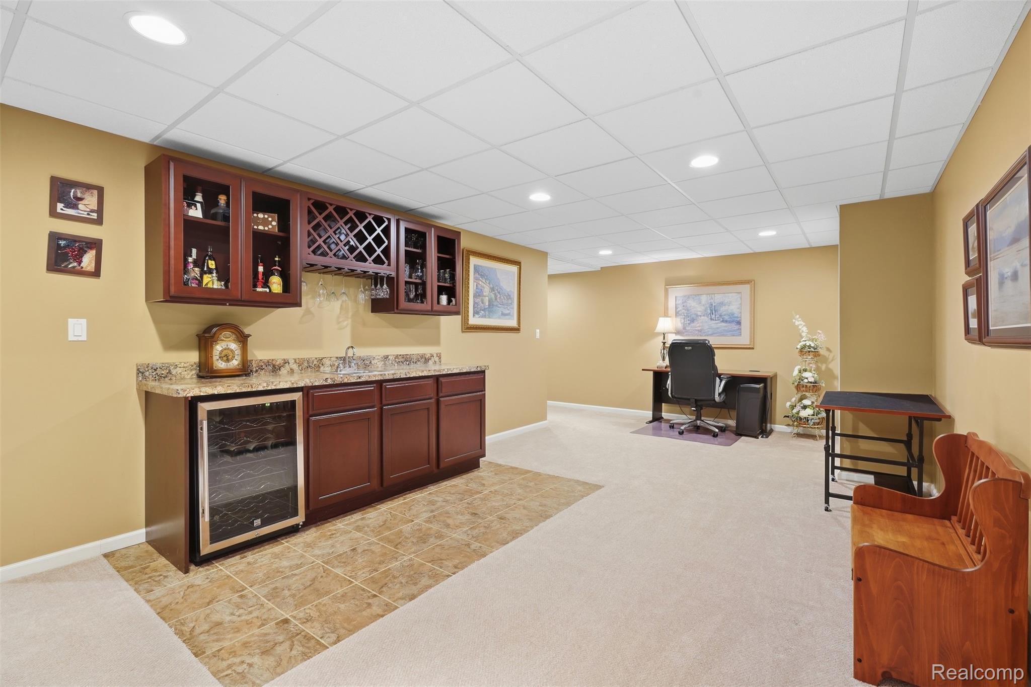 Furnished basement with a built-in wooden bar, wine refrigerator, and desk area.